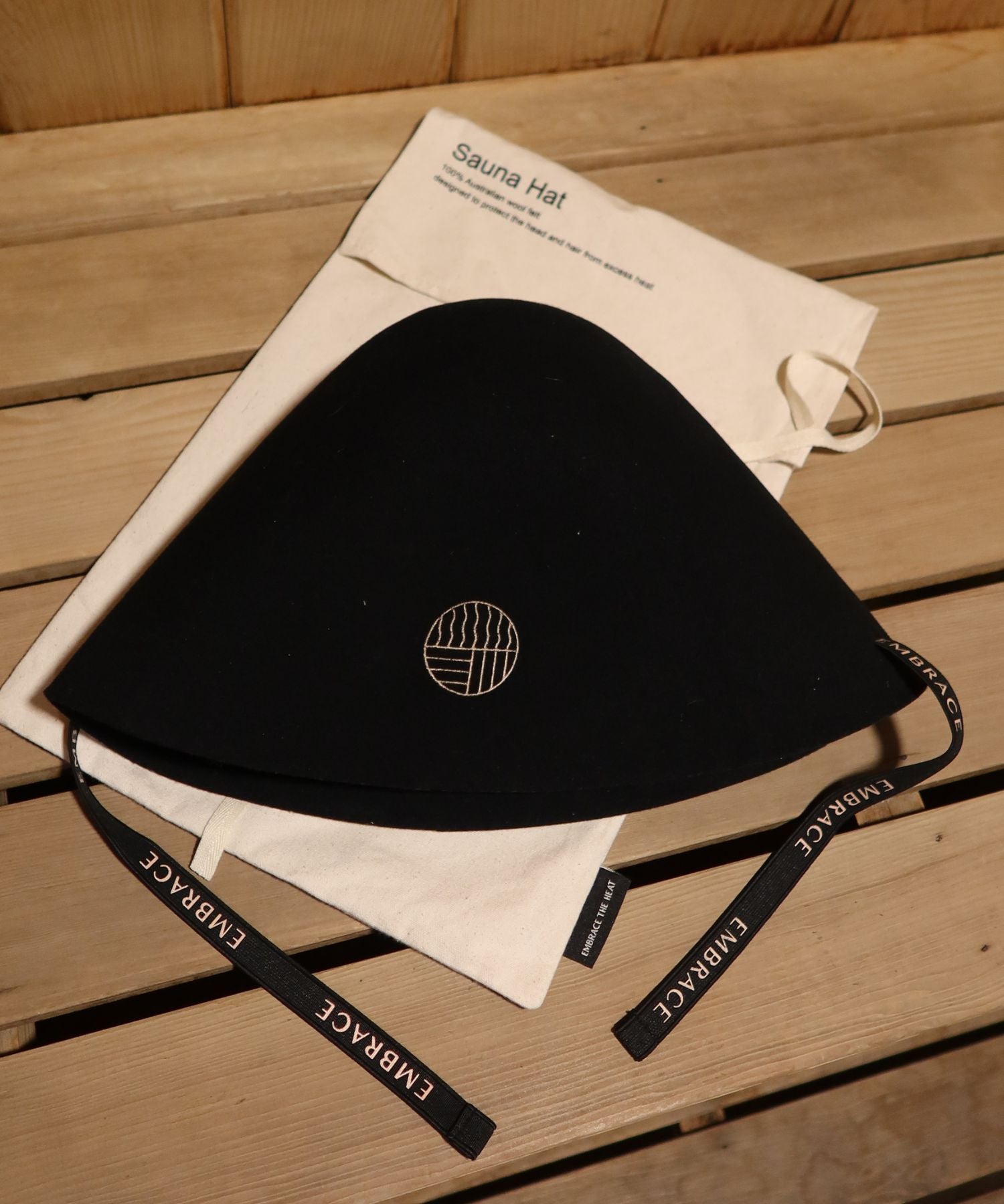 Premium black sauna hat made from 100% Australian merino wool with cotton storage bag in a traditional sauna.