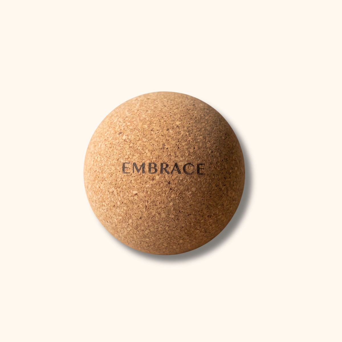 A round cork massage ball with the word 'EMBRACE' printed in black text on its surface, set against a solid cream-colored background.